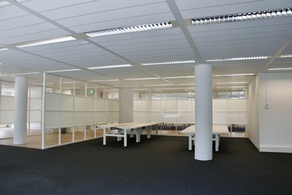 Modern open-plan office space at Koningin Wilhelminaplein with white desks and glass partition walls.